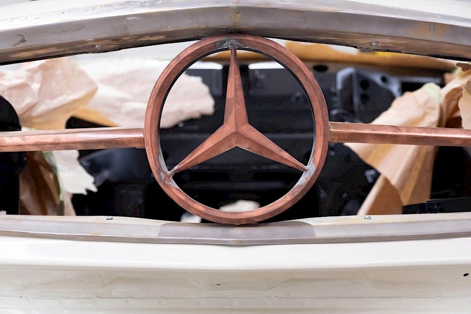 Zbliżenie na miedziane logo kierownicy w klasycznym projekcie restauracji Mercedesa, prezentujące rzemiosło i luksusowy design motoryzacyjny